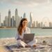 Liana sitzt mit Laptop am Strand von Dubai als Symbol für Online Business, Freiheit und ortsunabhängiges Arbeiten als Mama.