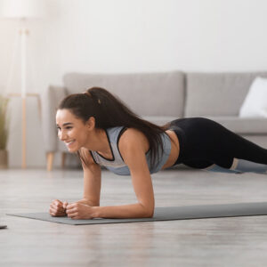 Frau macht eine Plank-Übung auf einer Matte vor dem Laptop als Symbol für täglich planken, Core Training und 60 Sekunden Fitnessroutine.