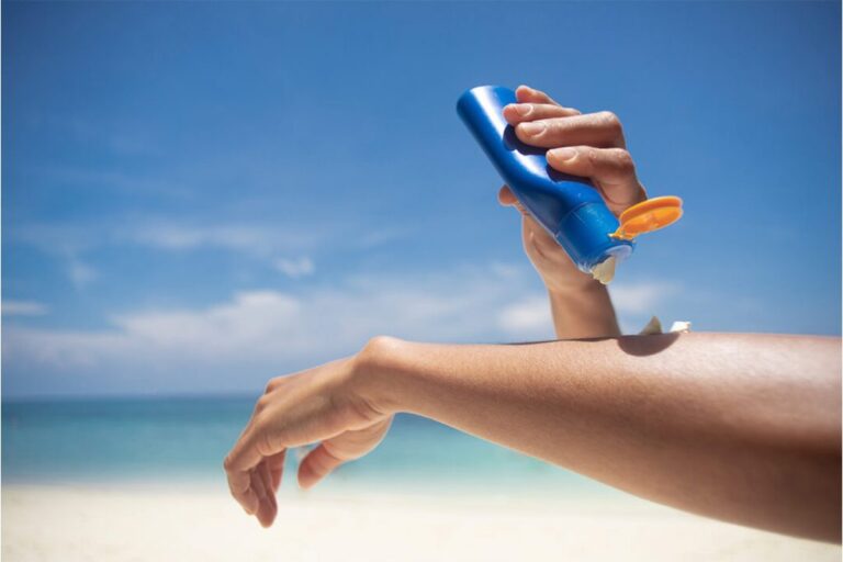 Frau trägt Sonnencreme am Strand auf die Schulter auf als Symbol für Sonnenschutz Mythen, LSF und richtige UV-Pflege im Alltag.